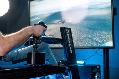 Person using a flight simulator with a joystick and screen displaying an aerial view.